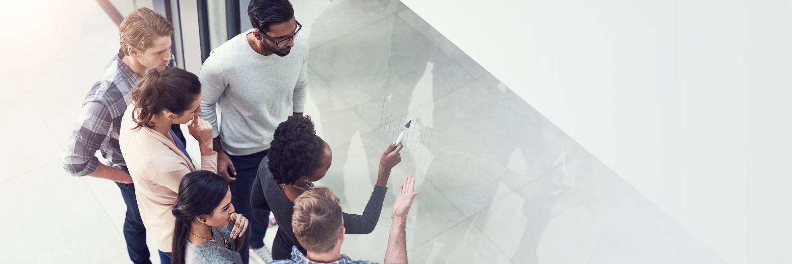 An overhead view of workshop participants working together at a large whiteboard.