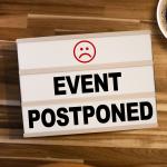 light box with the words "event postponed" on wooden table background