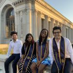 four graduate students sit in front of the UC Berkeley library wearing graduation sashes