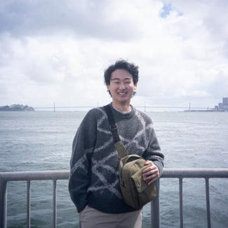 David Lee standing in front of the ocean wearing a grey sweater