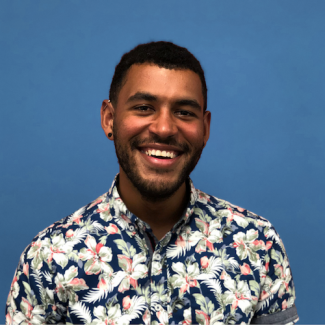 a picture of a smiling man with brown skin and a floral shirt