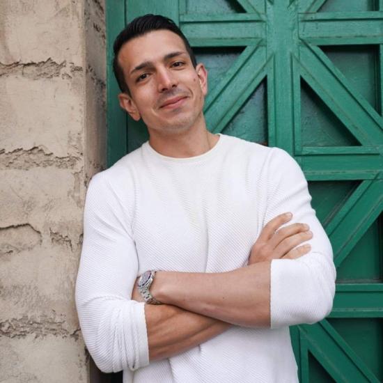 man in white shirt standing in front of green door, arms crossed