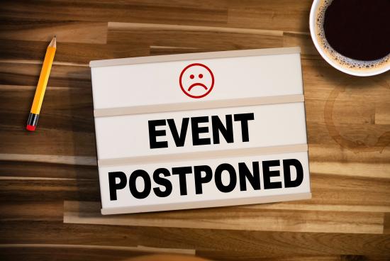 light box with the words "event postponed" on wooden table background