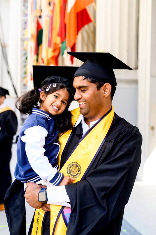 a graduate holds a small child smiling 